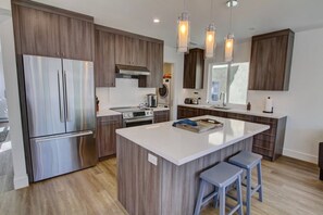 A modern kitchen with a central island, stainless steel appliances, wooden cabinetry, and pendant lighting. - Stylish home Rooftop HotTub 2Bd2Bth,Pet okay 2 Car (Newport Beach)