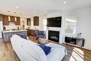 A modern living room with a sofa, a TV, a fireplace, and a kitchen area. - Stylish home Rooftop HotTub 2Bd2Bth,Pet okay 2 Car (Newport Beach)