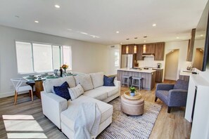 A modern living room with a sofa, ottoman, and chairs, a dining area with a table and chairs, and a kitchen with a bar area. - Stylish home Rooftop HotTub 2Bd2Bth,Pet okay 2 Car (Newport Beach)