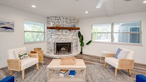 Una sala de estar moderna con chimenea de piedra, mobiliario de mimbre y ventanas amplias.