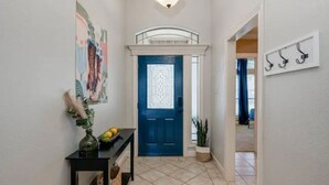A hallway with a blue door, a black console table with a vase and fruit, and a wall-mounted coat rack. - 8min Texas A&M, 1 King Beds, firepit, GriddleGrill (College Station)