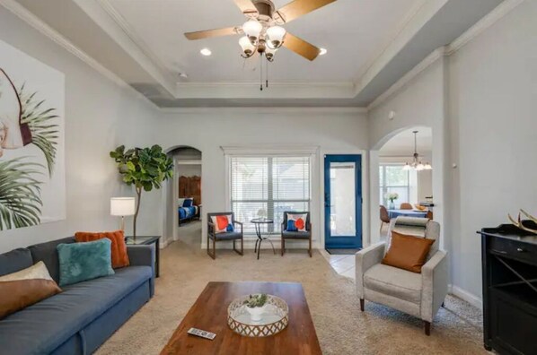 A spacious living room with a ceiling fan, a blue sofa, a coffee table, and a door leading to another room.