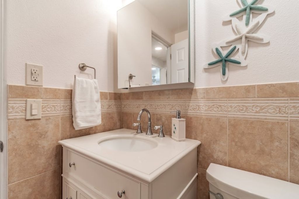 Un baño con un lavamanos blanco, un espejo y decoración de estrellas de mar en la pared.