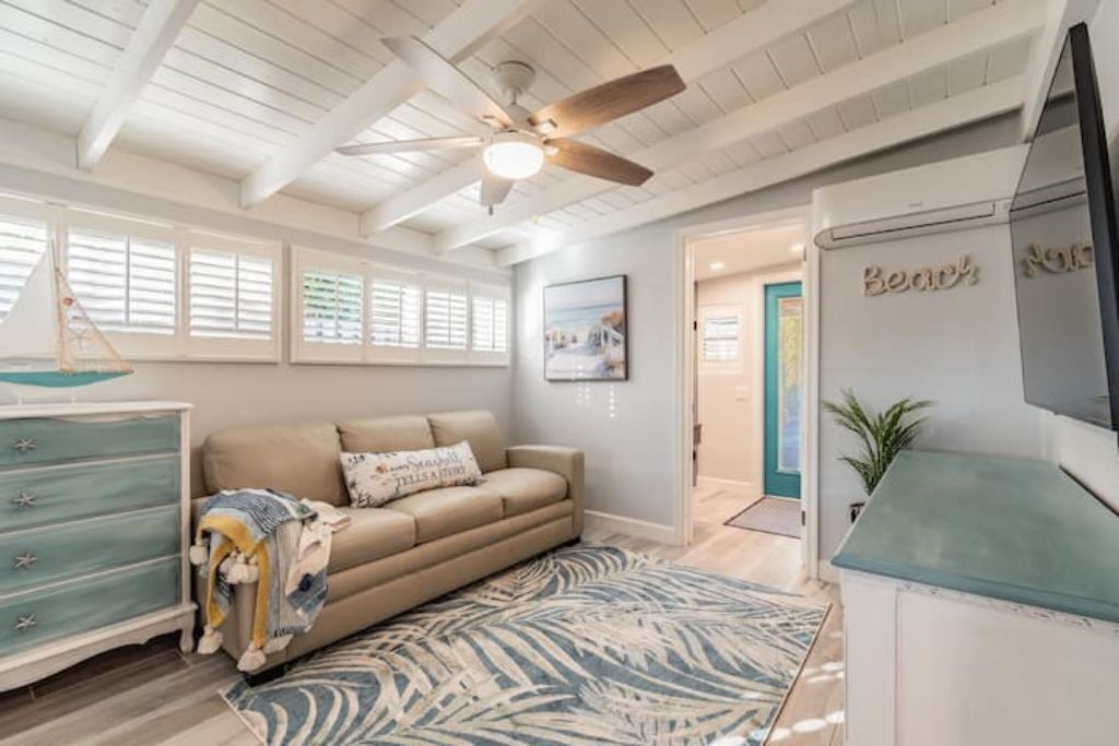 A room with a ceiling fan, a sofa, a patterned rug, a dresser, and a television.