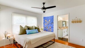 A bedroom with a bed, a ceiling fan, a window with blinds, a bathroom visible through an open door, and a wall-mounted towel rack. - River, Wine, Hot Tub, 2 King Beds, Large backyard (Blanco)