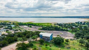 A large house with a blue roof and white walls, surrounded by trees and a body of water. - 5 kings, 3 acres, lake view, cabana, firepit/stars (Buchanan Dam)