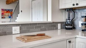 A kitchen with white cabinets, a patterned backsplash, a coffee maker, and a cutting board with a knife. - 5 kings, 3 acres, lake view, cabana, firepit/stars (Buchanan Dam)
