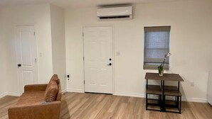 Una habitación con un sofá de cuero marrón, una mesita de madera con una planta en maceta y una puerta blanca.
