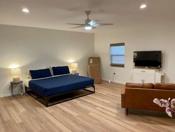 A bedroom with a bed, bedside lamps, a ceiling fan, a TV, a cabinet, and a window.