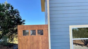 Un portón de madera con tres paneles de vidrio, una casa azul con revestimiento horizontal y una ventana con marco blanco.