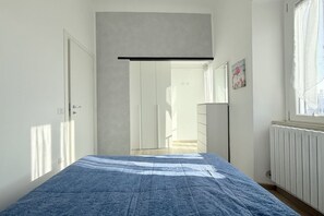 A bedroom with a bed, a wardrobe, a radiator, and a window.