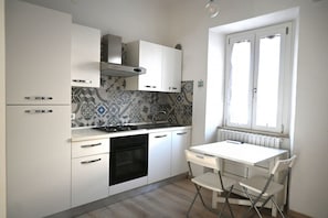Een keuken met witte kastjes, een gasfornuis, een oven en een raam met zonwering.