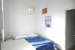 Een slaapkamer met een bed, een hanglamp, een klein raam en een aan de muur bevestigd schilderij.