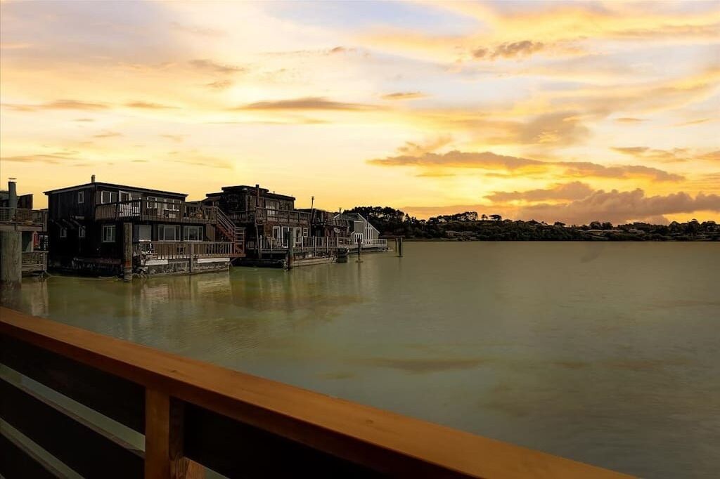 A waterfront property with a wooden deck, a staircase leading to a second floor, and a view of the water.