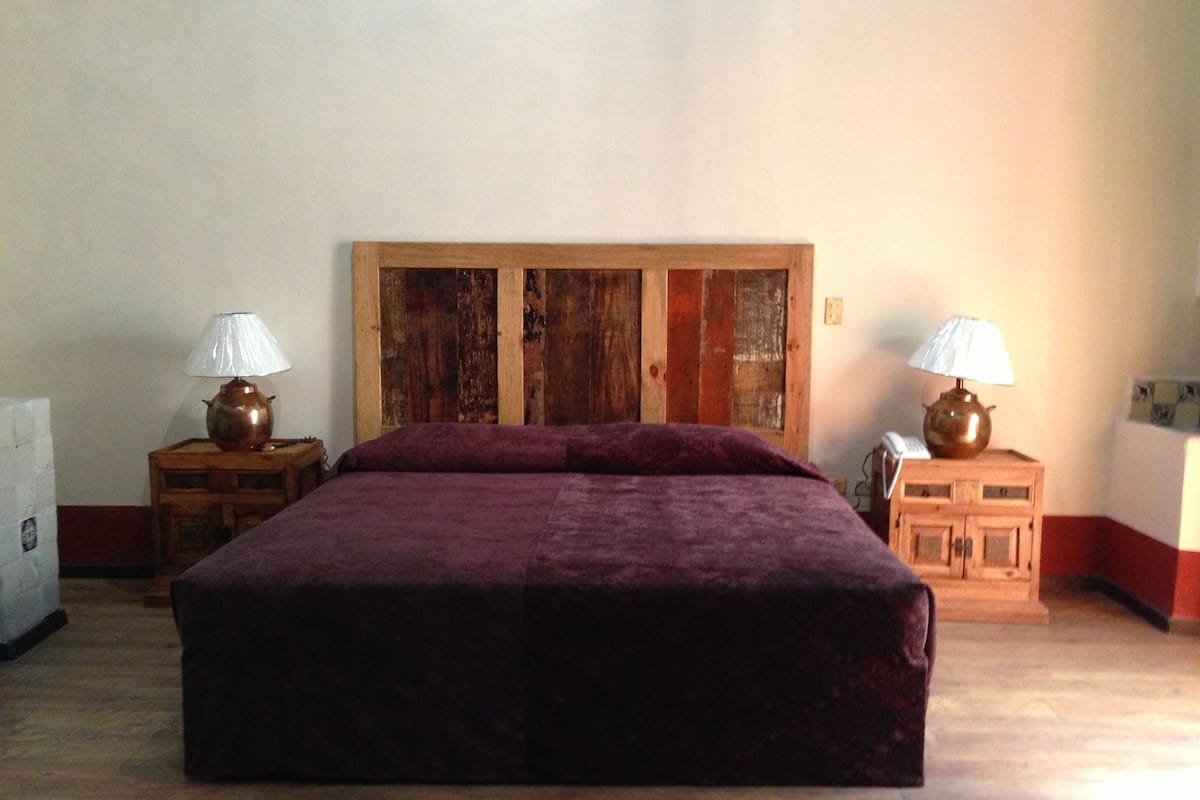 Un dormitorio con una cama grande, cabecera de madera, dos mesitas de noche con lámparas y un mueble pequeño.
