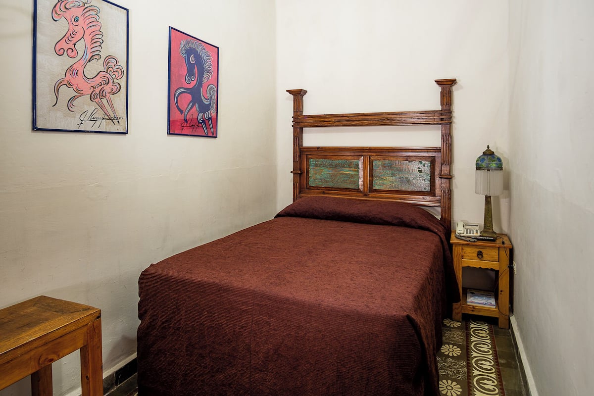 Un dormitorio con cama de madera, una mesita de noche con lámpara y dos cuadros en la pared.
