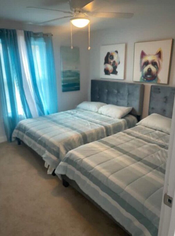 Une chambre avec deux lits, un ventilateur de plafond et des œuvres d’art accrochées aux murs.