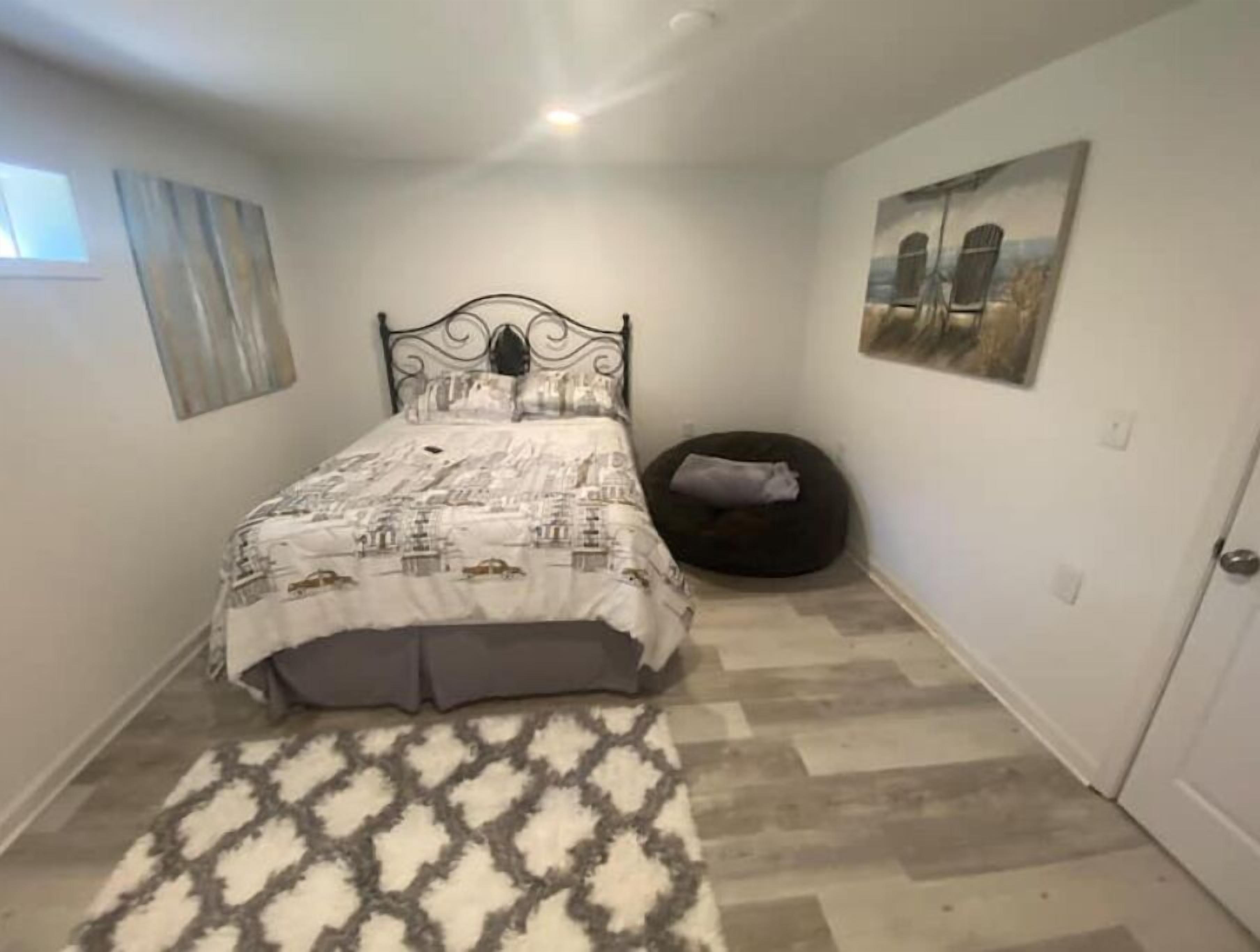 Un dormitorio con una cama, un tapete, un sillón de peluche y un cuadro en la pared.