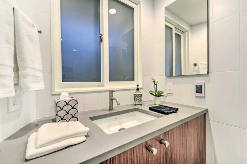 A modern bathroom with a grey countertop, a white sink, a mirror, and a wooden cabinet.