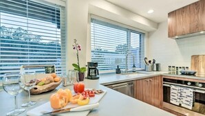 Een moderne keuken met een groot eiland, roestvrijstalen apparatuur en uitzicht door de ramen.