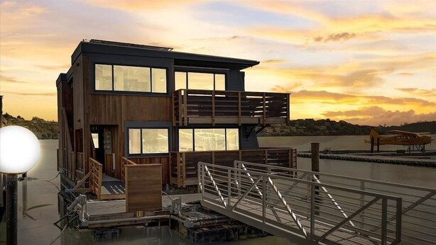 Een modern meerlaags gebouw met grote ramen, een houten gevel en een steiger die in het water uitkomt.