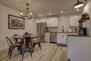 Una cocina moderna con armarios blancos, electrodomésticos de acero inoxidable y una zona de comedor con una mesa redonda y sillas.