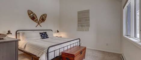 A bedroom with a bed, a wooden chest, a wall-mounted decoration, and a window.