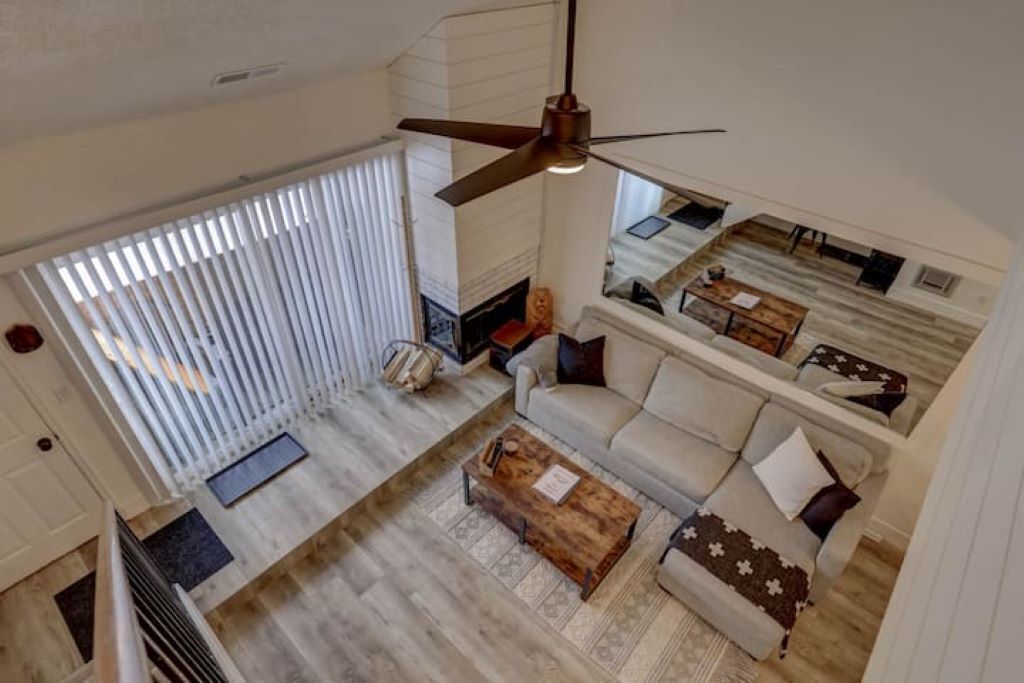 Un vaste espace de vie doté d’un haut plafond, d’un ventilateur de plafond, d’une grande fenêtre avec stores, d’un ensemble de canapés et d’une table basse.