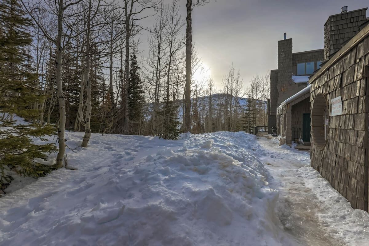 Un sendero cubierto de nieve que lleva a un edificio con fachada de madera y una chimenea.