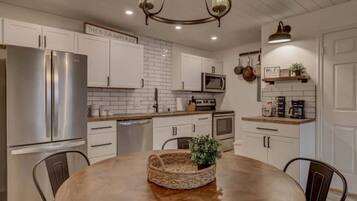 A modern kitchen with white cabinets, stainless steel appliances, and a wooden dining table.