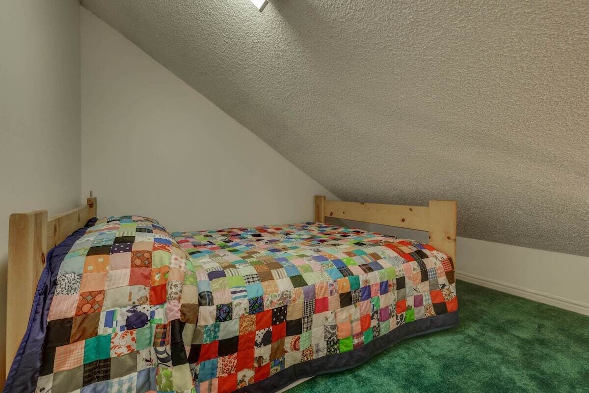 Una habitación pequeña con cama individual, cabecero de madera y colcha colorida de retazos.