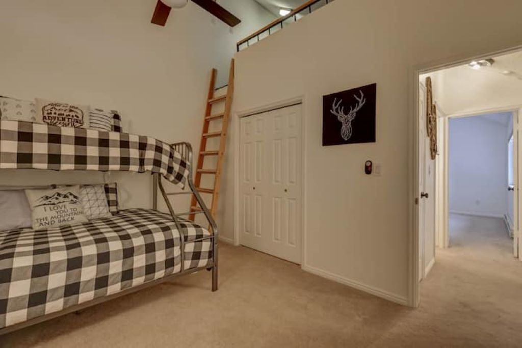 Een slaapkamer met een stapelbed, een ladder, een deur en een muur met een hertentapijt.
