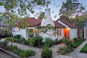 A single-story house with a red-tiled roof, a chimney, and a well-maintained garden with various plants and a pathway leading to the entrance.