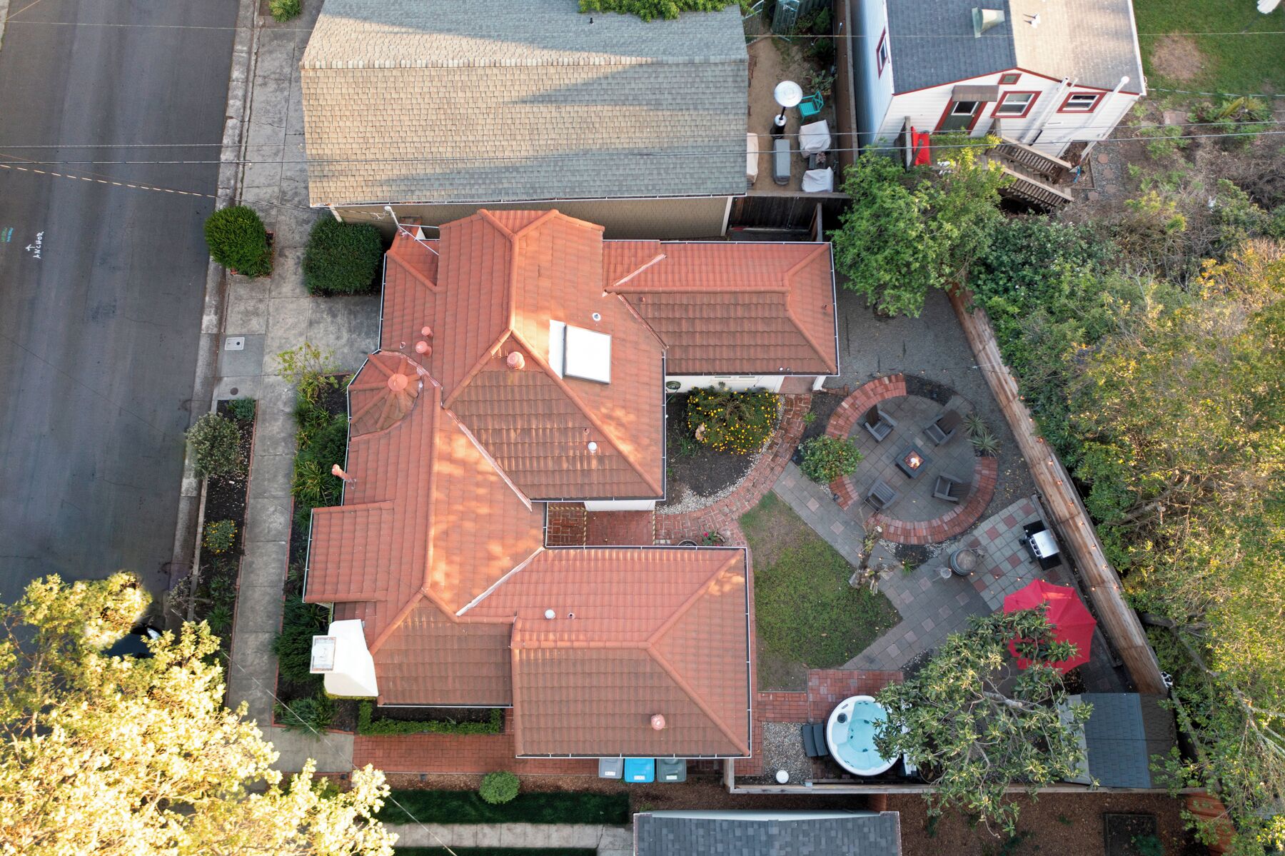 An aerial view of a residential property with a red-tiled roof, a fenced backyard with a patio, and a swimming pool.
