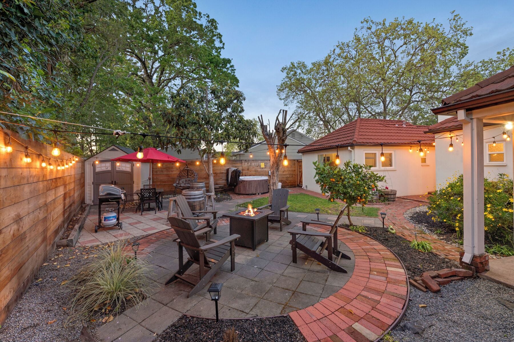 A backyard with a fire pit, outdoor furniture, and string lights.