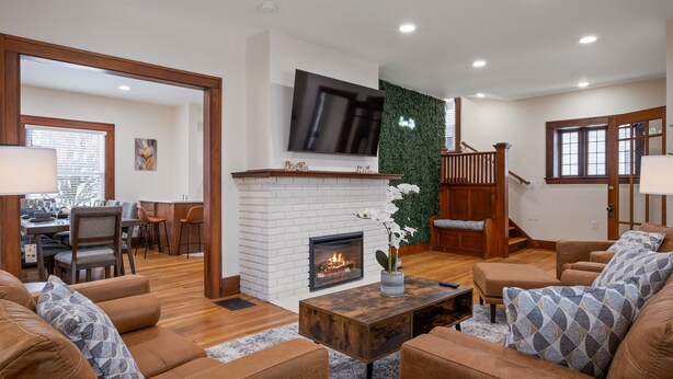 A spacious living room with a fireplace, comfortable seating, and a television mounted on the wall. - Eastown Luxe (Grand Rapids)