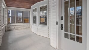 A covered patio area with white siding, a brick wall, and a wooden ceiling. - Eastown Luxe (Grand Rapids)