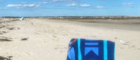 Una playa con una silla de playa azul y blanca y un taburete de madera.