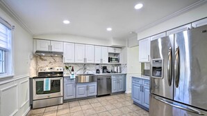 A modern kitchen with stainless steel appliances, white cabinets, and a tiled floor. - Bay Shore Vacation Rental w/ Shared Yard! (Bay Shore)
