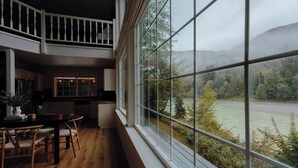 Ein großzügiger Essbereich mit hoher Decke und Blick auf Fluss und Wald durch große Fenster.