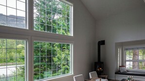 A spacious living room with large windows, a fireplace, and a dining area. - Riverside Retreat - Skagit River with hot tub, fire pit, views (Concrete)