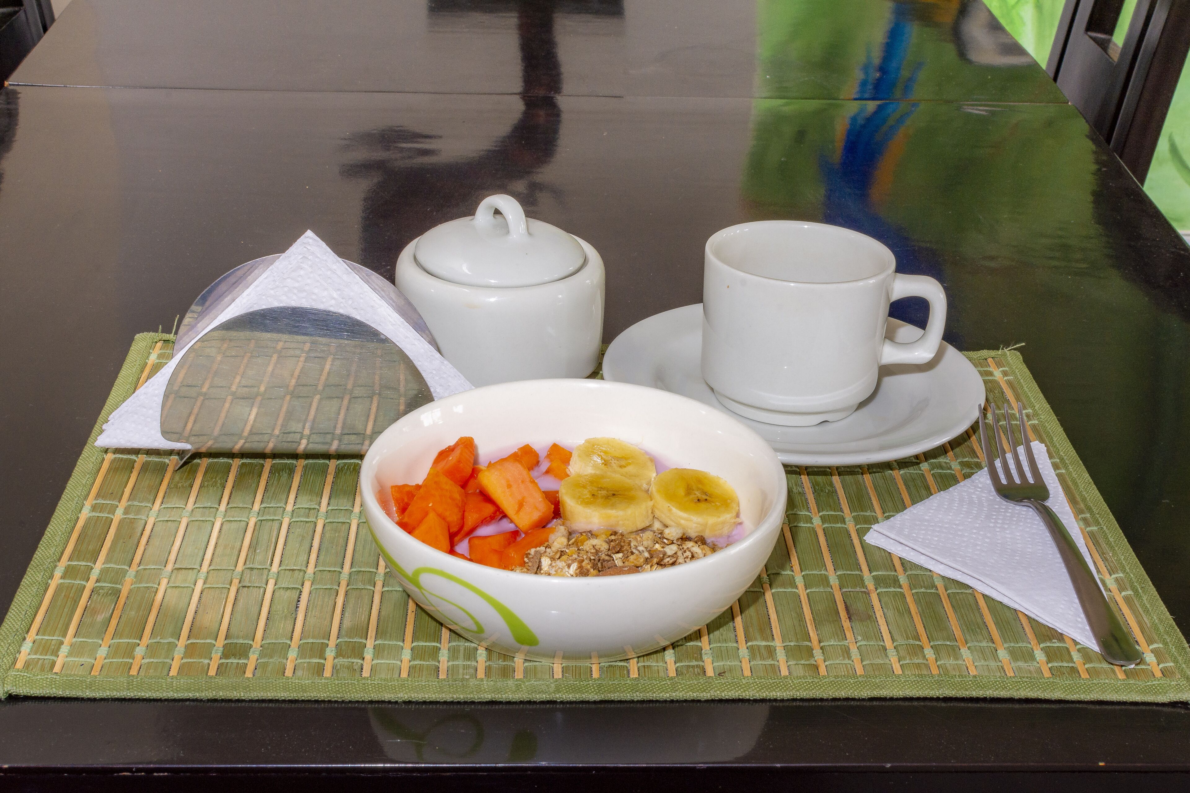 Une table dressée pour le petit-déjeuner, avec un bol de céréales, des bananes et des carottes, une théière, une tasse et une soucoupe.