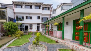Un patio con un jardín pequeño, un edificio blanco con múltiples ventanas y una puerta verde con detalles rojos.