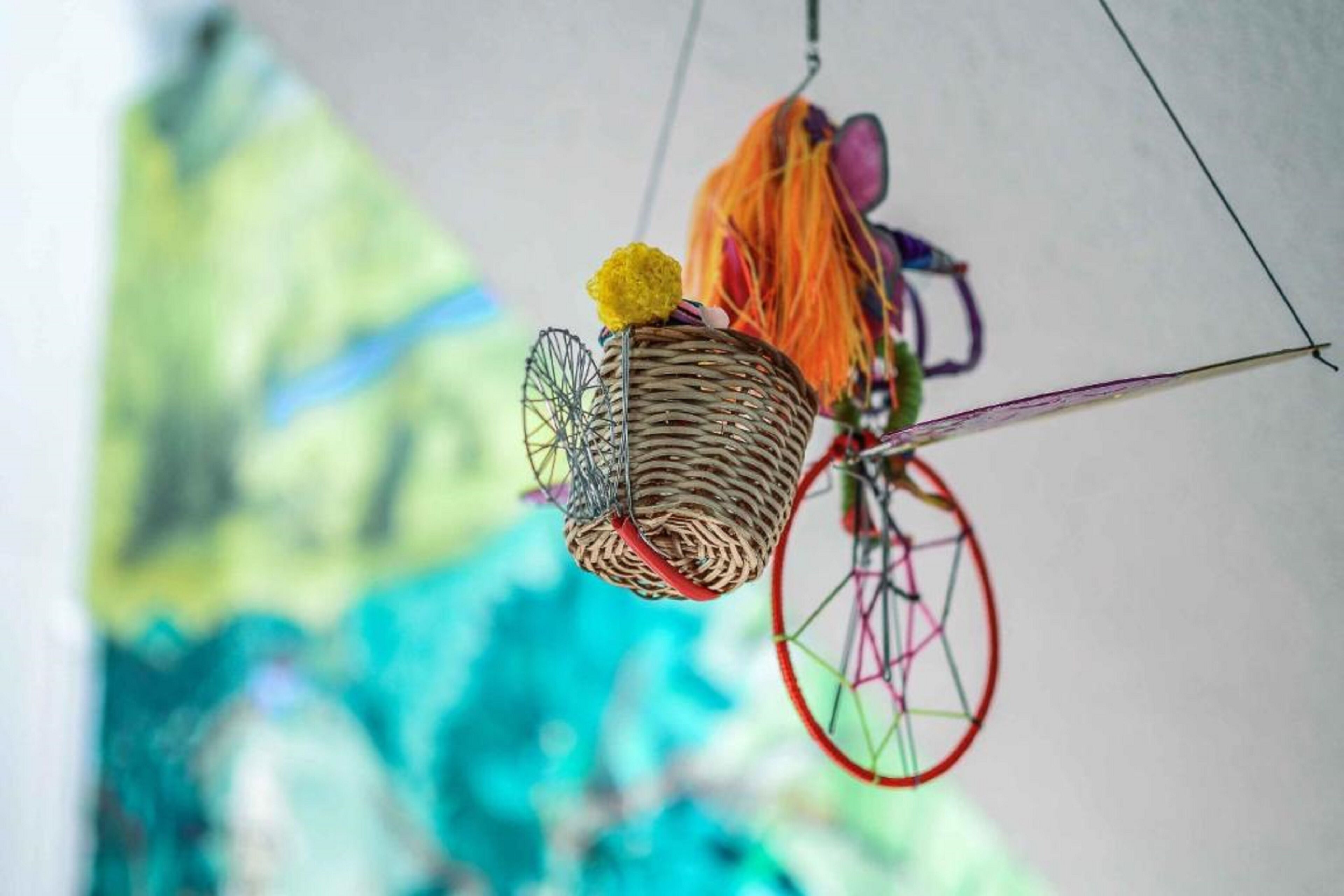 A wicker basket with a yellow pom-pom, hanging from a bicycle wheel.