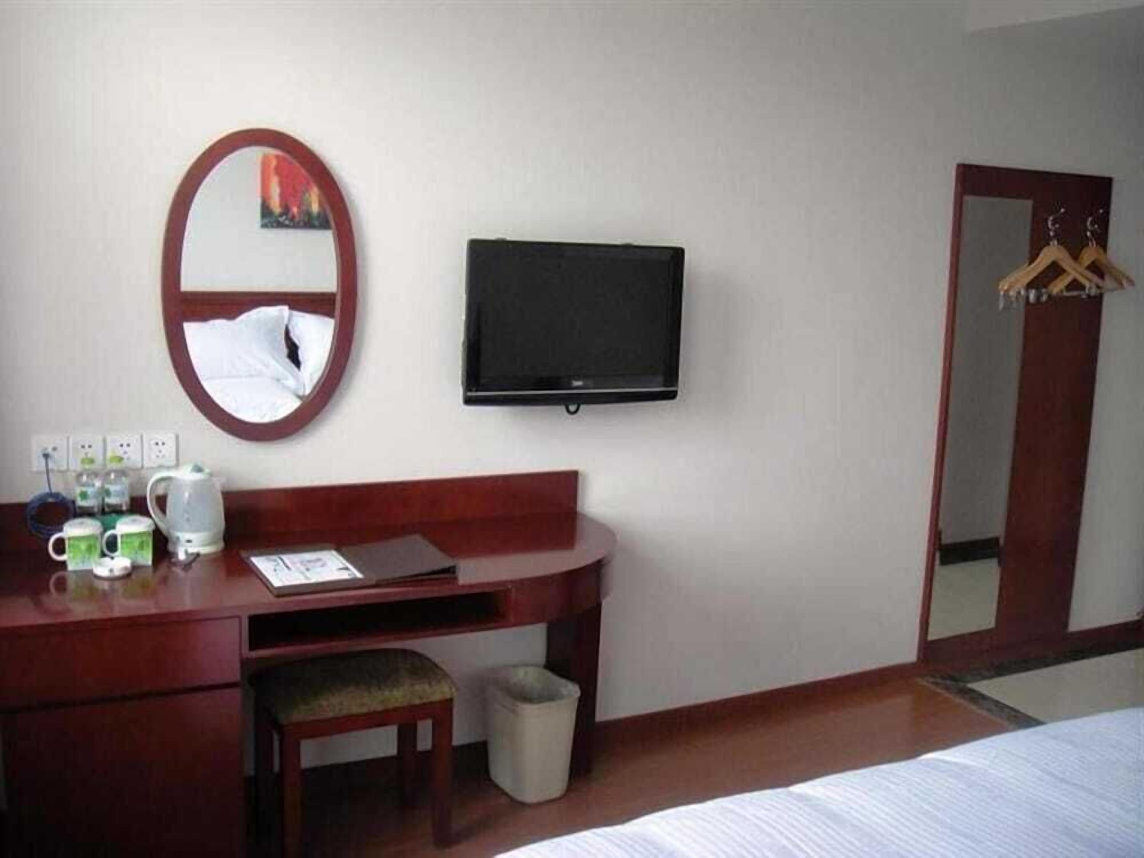 Quarto de hotel com uma escrivaninha de madeira, televisão, espelho, cama e guarda-roupa.