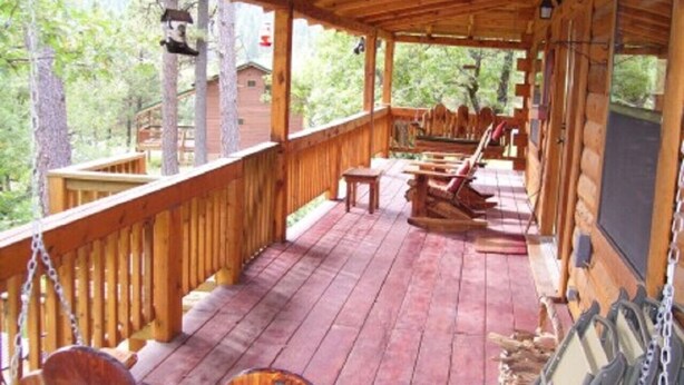Une terrasse en bois, agrémentée de chaises et de tables, entourée d’arbres.