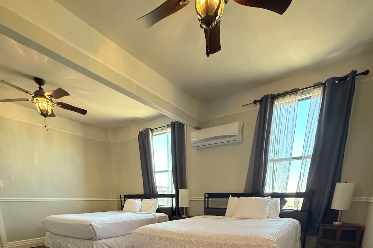 Hotelkamer met twee bedden, een plafondventilator, een airconditioningssysteem en een raam met gordijnen.