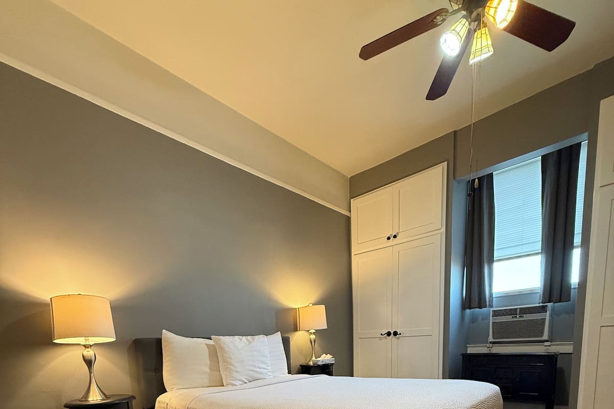 Een slaapkamer met een bed, twee nachtkastjes met lampen, een plafondventilator en een kledingkast.