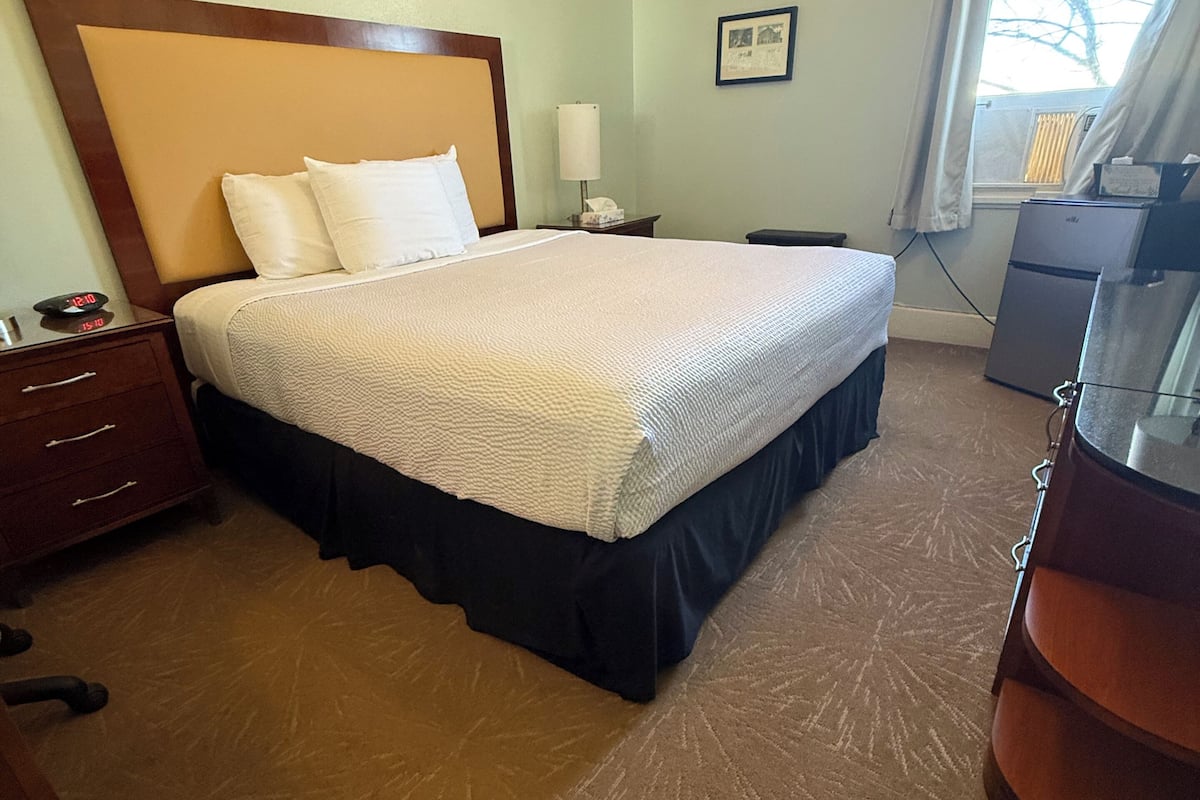 Een hotelkamer met een groot bed, een nachtkastje, een bureau, een stoel en een raam met gordijnen.
