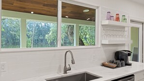 Una cocina moderna con un amplio ventanal, armarios blancos y un lavamanos de acero inoxidable.